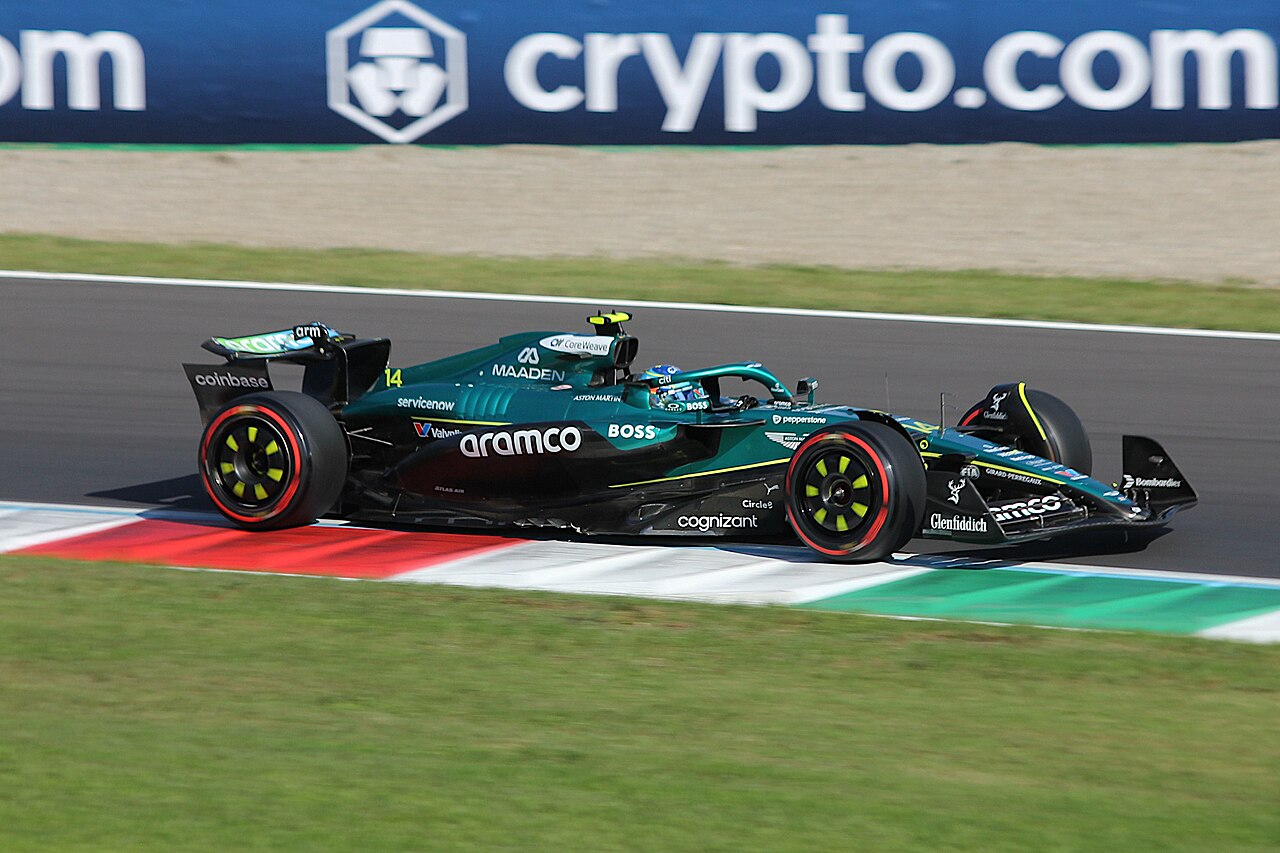 Fernando Alonso's green Aston Martin on track beside a red and white kerb