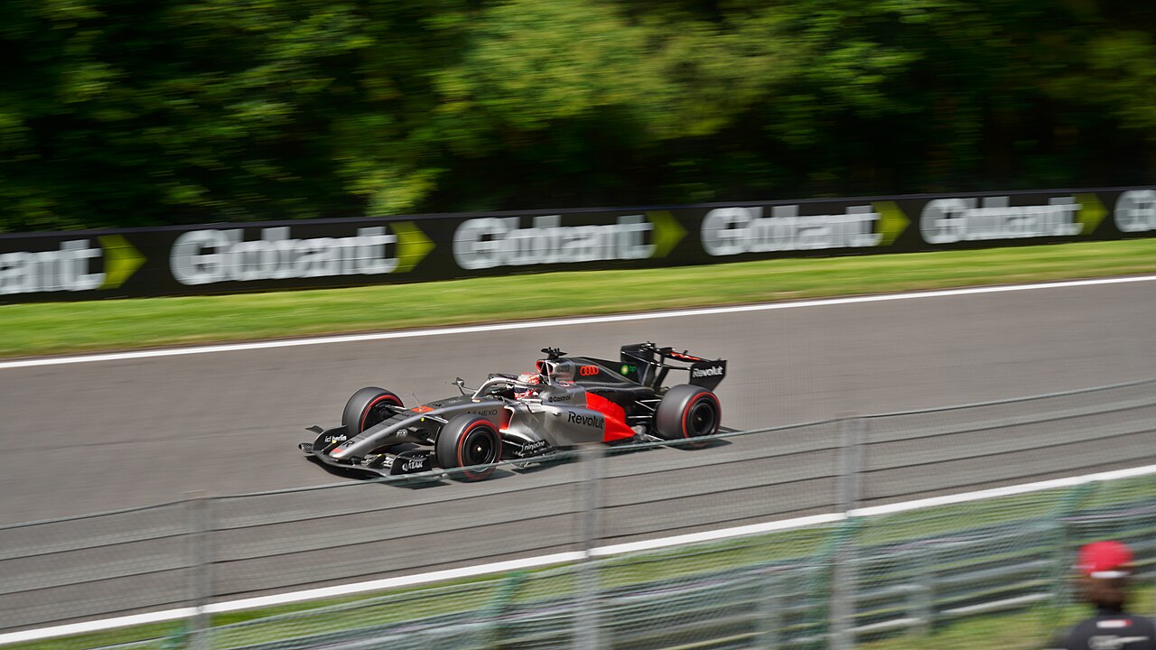 Nico Hülkenberg's black, silver and red Audi F1 car at speed past a line of trackside advertising boards