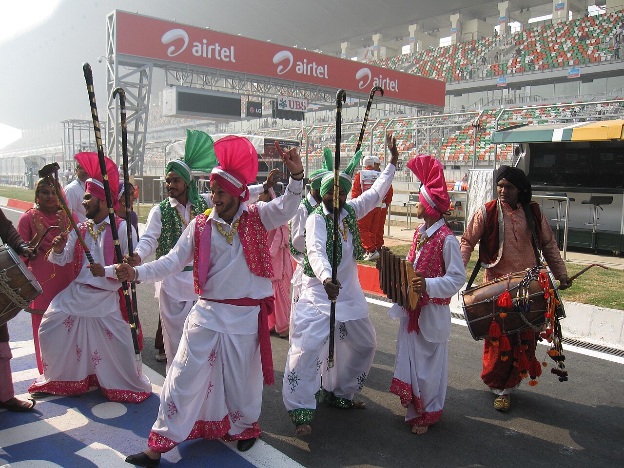 Dancers in white and pink costumes with colourful turbans performing on the grid in front of a grandstand